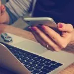 woman holding phone while working on pc